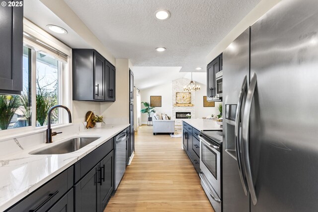 kitchen featuring appliances with stainless steel finishes, a fireplace, light wood finished floors, a sink, and a textured ceiling