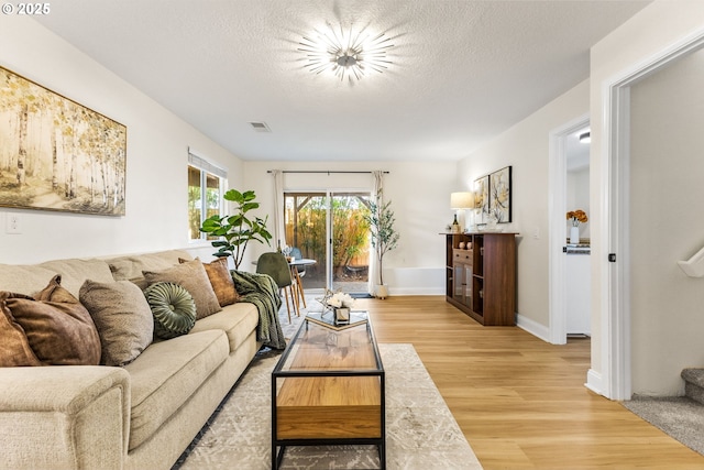 living area with baseboards, visible vents, light wood-style floors, and a textured ceiling