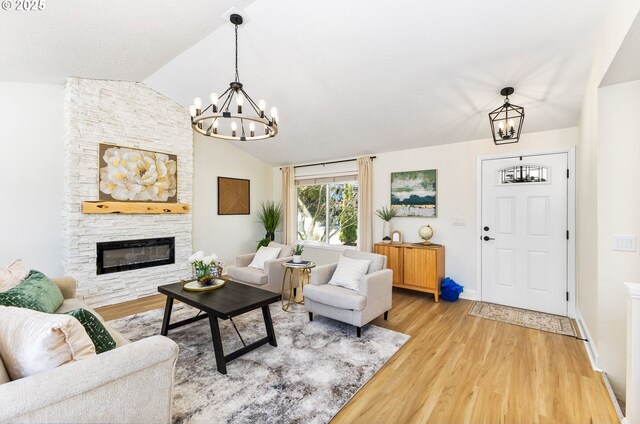 living room with light wood-style floors, vaulted ceiling, a stone fireplace, baseboards, and a notable chandelier
