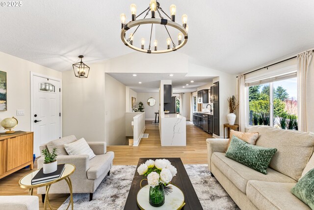 living area featuring light wood-style floors, a healthy amount of sunlight, a notable chandelier, and vaulted ceiling