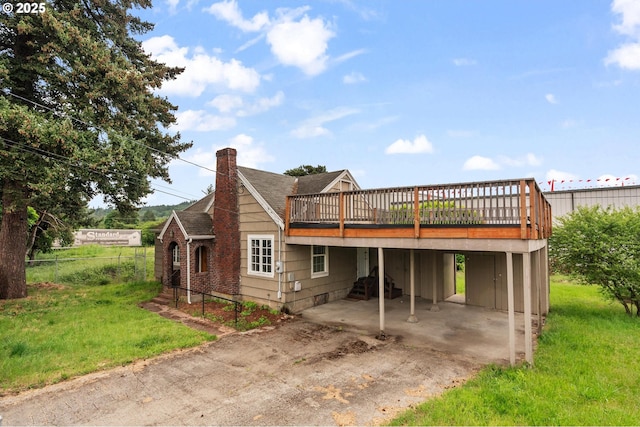 back of house featuring a wooden deck, concrete driveway, a chimney, a patio area, and a carport