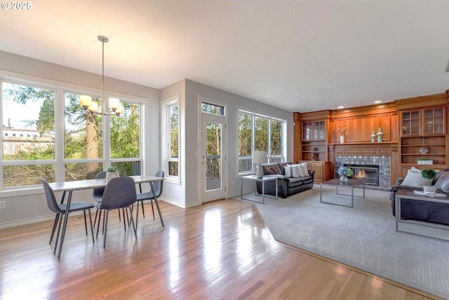 living room with a tiled fireplace, light hardwood / wood-style flooring, a chandelier, and plenty of natural light