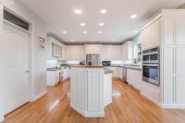 kitchen featuring sink, white cabinetry, stainless steel appliances, a center island, and light wood-type flooring