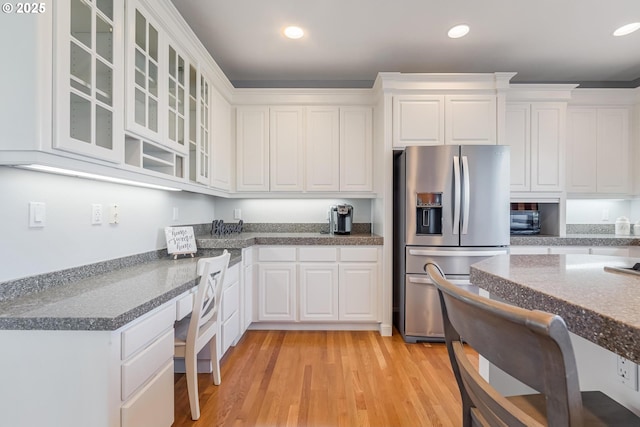 kitchen with stainless steel refrigerator with ice dispenser, built in desk, white cabinets, and light hardwood / wood-style floors