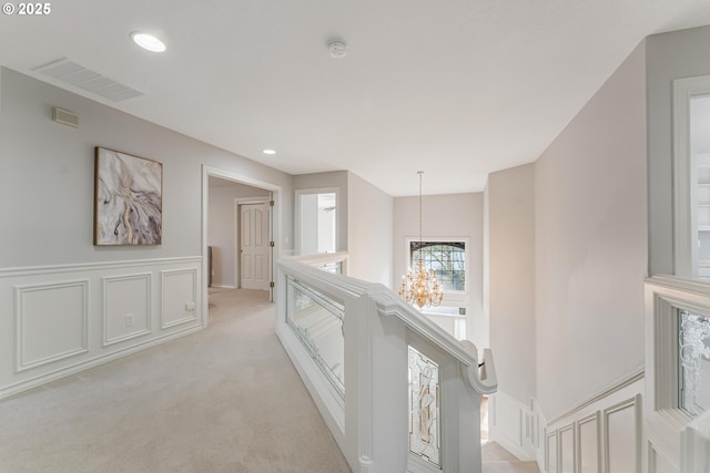 hallway with light carpet and an inviting chandelier