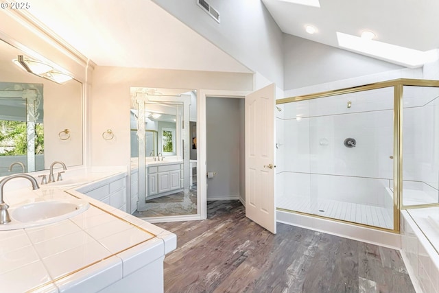 bathroom featuring vanity, hardwood / wood-style flooring, plus walk in shower, and vaulted ceiling with skylight