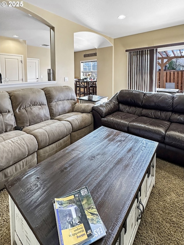 living area featuring recessed lighting, arched walkways, and dark colored carpet