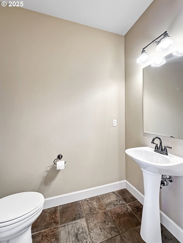 bathroom featuring toilet, baseboards, and a sink