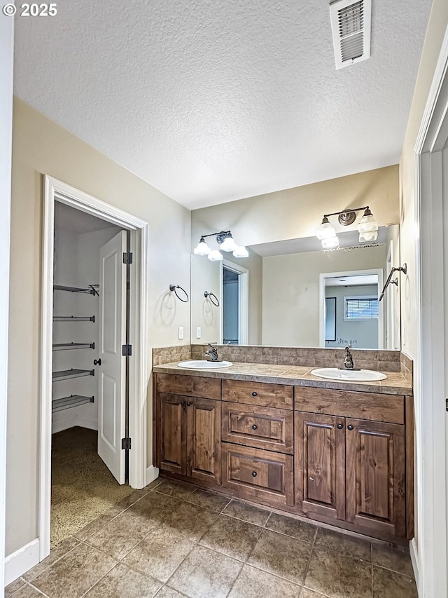 bathroom with double vanity, visible vents, a walk in closet, and a sink