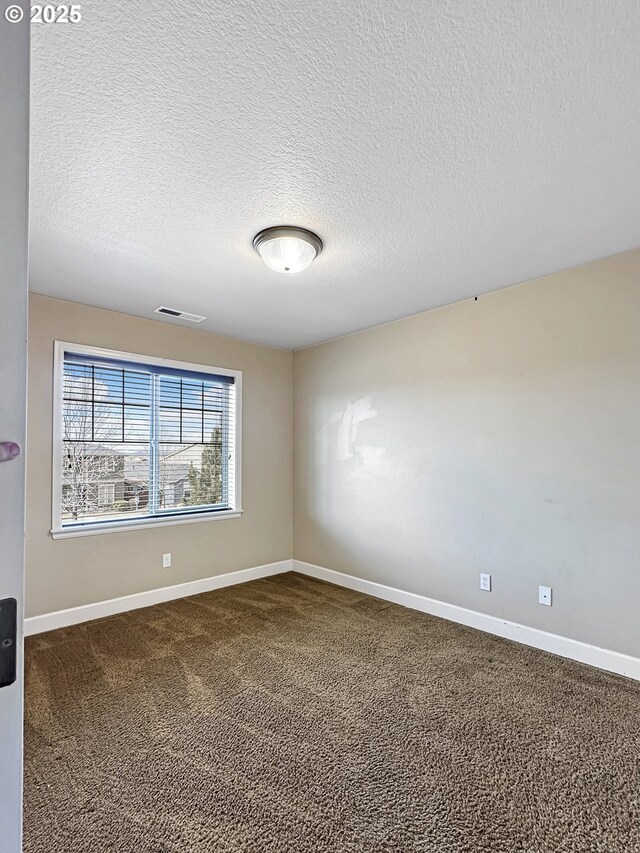 unfurnished room with visible vents, dark carpet, a textured ceiling, and baseboards