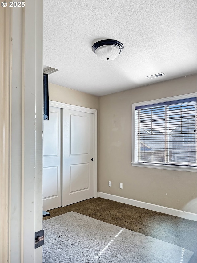 unfurnished bedroom featuring visible vents, baseboards, carpet floors, a closet, and a textured ceiling