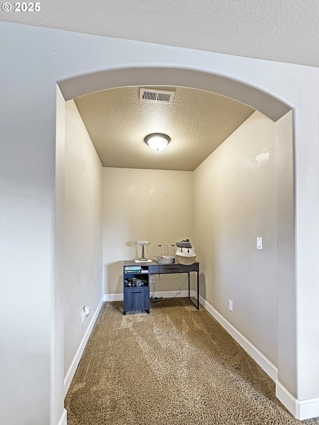 unfurnished office featuring carpet, visible vents, baseboards, arched walkways, and a textured ceiling