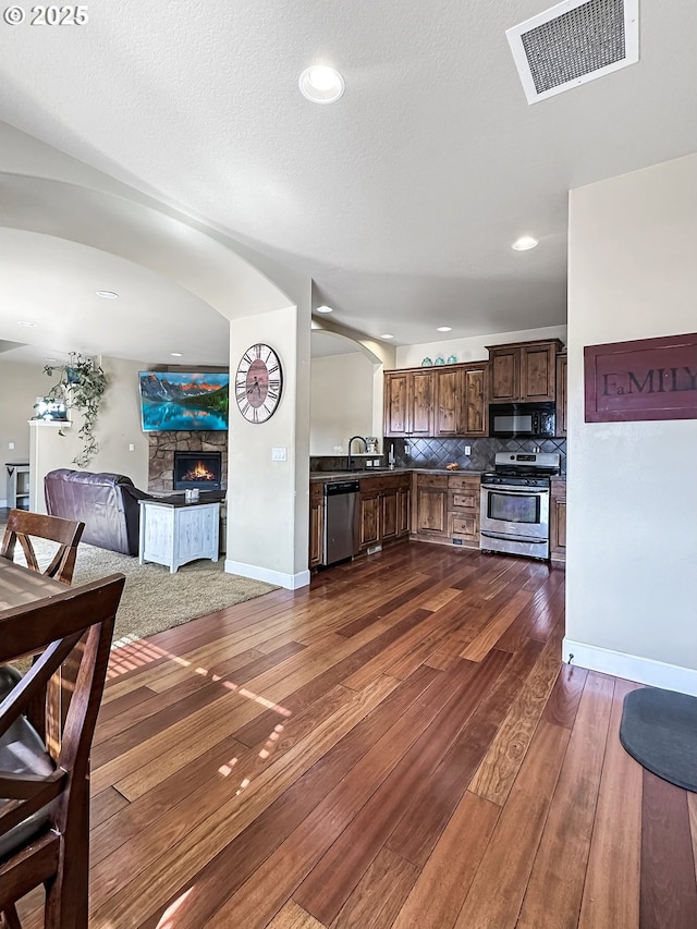 kitchen with dark countertops, visible vents, dark wood-type flooring, a stone fireplace, and stainless steel appliances