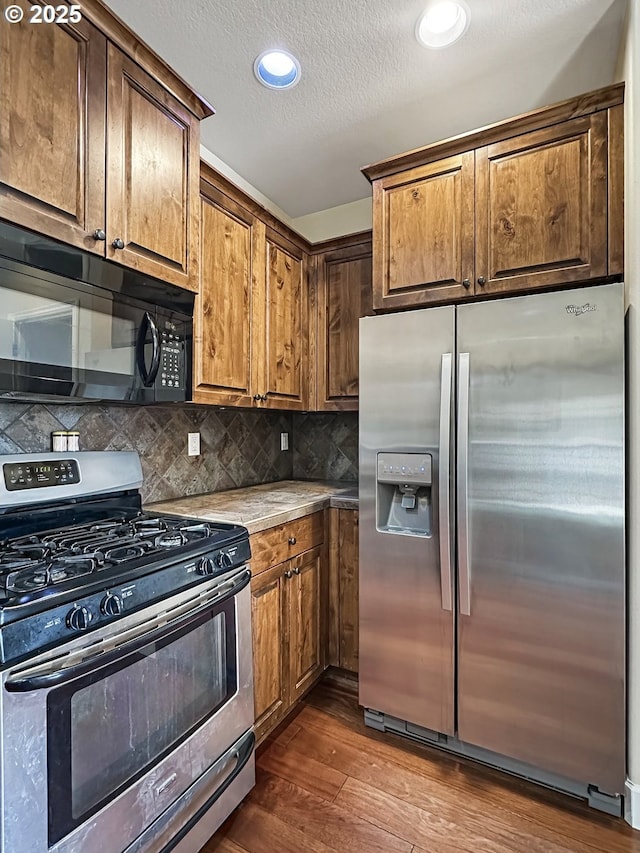 kitchen featuring a textured ceiling, stainless steel appliances, light countertops, decorative backsplash, and dark wood-style flooring