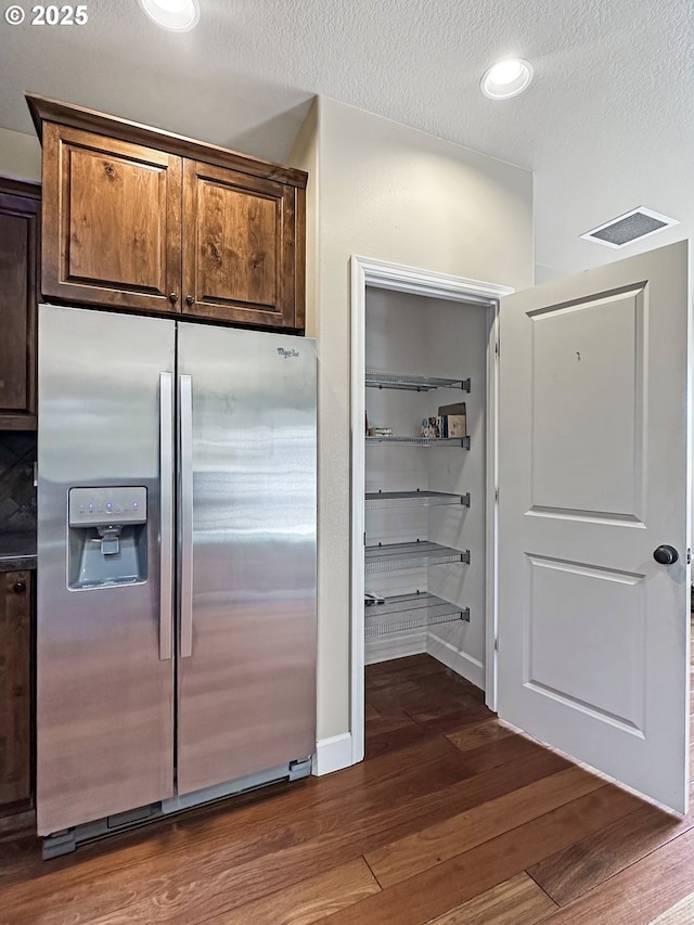 kitchen with visible vents, dark wood-type flooring, baseboards, stainless steel fridge, and a textured ceiling