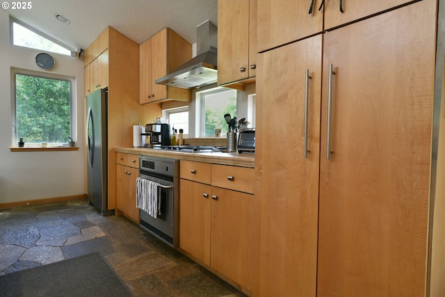 8302 SW 65th Ave, Portland, OR 97219 - kitchen featuring stainless steel appliances, wall chimney range hood, dark stone finish flooring, tile counters, and baseboards