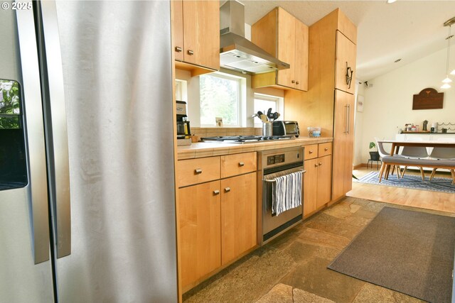 8302 SW 65th Ave, Portland, OR 97219 - kitchen with stainless steel appliances, wall chimney range hood, tile counters, vaulted ceiling, and decorative light fixtures