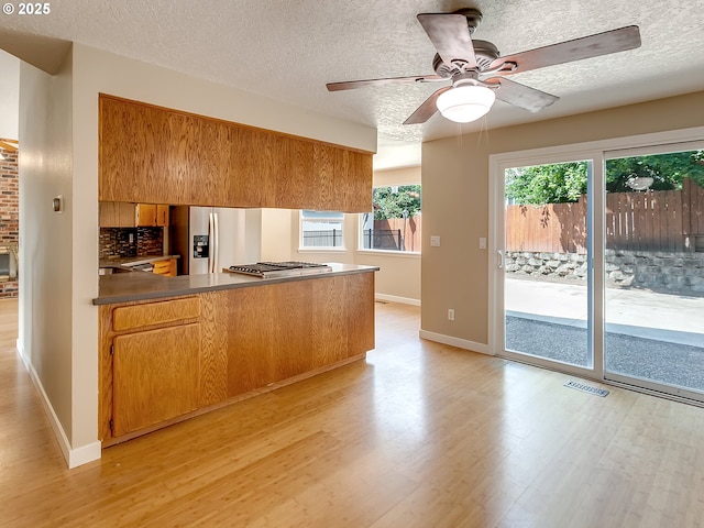 5367 NW 180th Pl, Portland, OR 97229 - kitchen featuring stainless steel appliances, a peninsula, brown cabinets, light wood-style flooring, and dark countertops