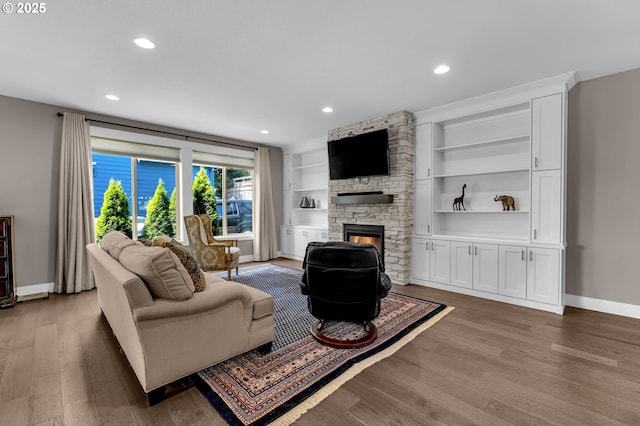 living room featuring a stone fireplace, baseboards, wood finished floors, recessed lighting, and built in features