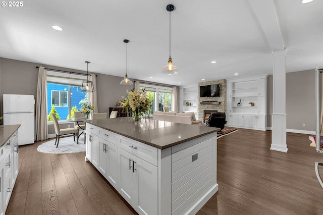 kitchen featuring decorative columns, freestanding refrigerator, dark countertops, dark wood-style floors, and a fireplace