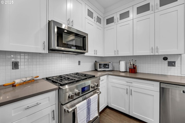 kitchen featuring appliances with stainless steel finishes, dark countertops, white cabinetry, and tasteful backsplash
