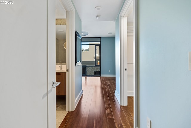hall featuring baseboards, a sink, and dark wood-style floors