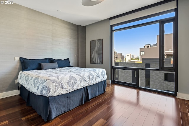 bedroom featuring baseboards, wallpapered walls, and dark wood-style floors