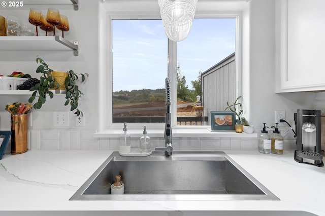 kitchen with a sink, white cabinets, light stone countertops, and open shelves