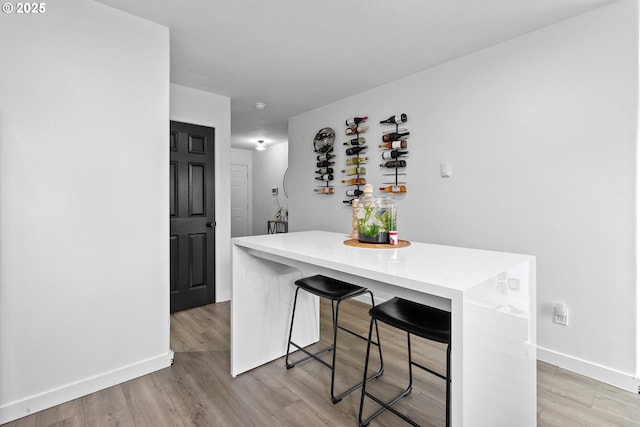 kitchen with baseboards, a breakfast bar area, light countertops, light wood-style flooring, and a center island