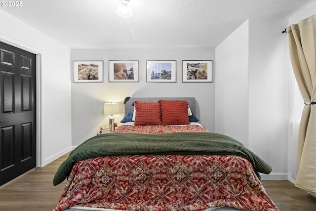 bedroom with wood finished floors, baseboards, and a textured ceiling