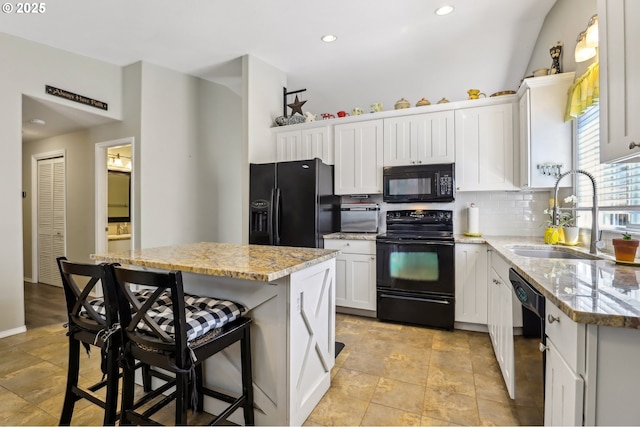 kitchen with a sink, black appliances, white cabinetry, decorative backsplash, and light stone countertops