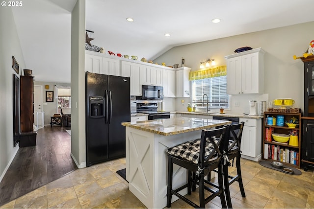 kitchen featuring a sink, black appliances, vaulted ceiling, white cabinetry, and light stone countertops