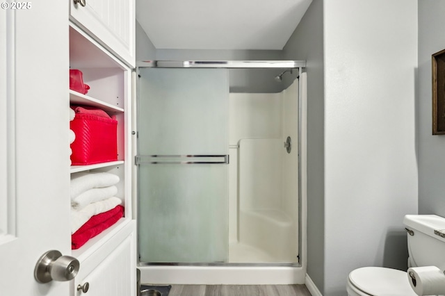 bathroom featuring toilet, baseboards, a shower stall, and wood finished floors