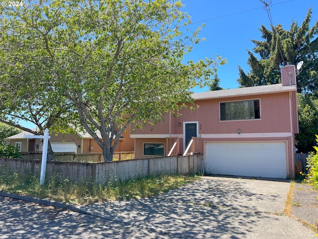 split foyer home featuring a chimney, fence, driveway, and an attached garage