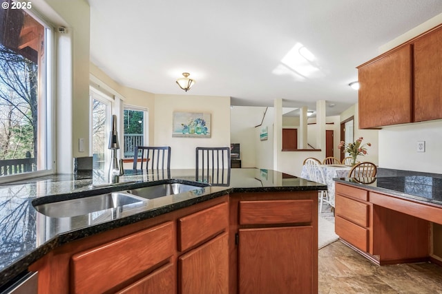 kitchen with brown cabinetry, dark stone counters, and a sink