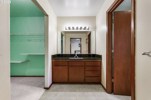 bathroom with a walk in closet, vanity, and baseboards