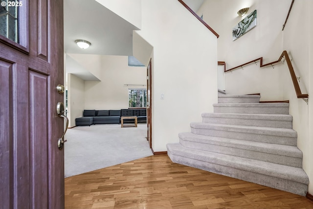 carpeted foyer entrance with stairs, a towering ceiling, and wood finished floors