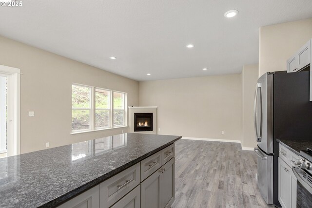 1516 Samuel Dr, Cottage Grove, OR 97424 - kitchen with light wood-style flooring, stainless steel appliances, dark stone counters, a glass covered fireplace, and recessed lighting