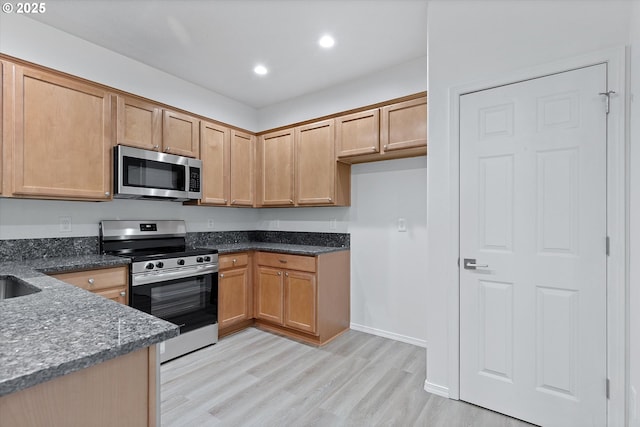 kitchen featuring light hardwood / wood-style floors, dark stone countertops, and appliances with stainless steel finishes