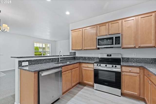 kitchen featuring pendant lighting, sink, dark stone countertops, kitchen peninsula, and stainless steel appliances