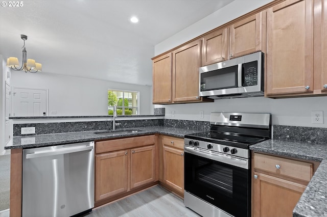 kitchen featuring appliances with stainless steel finishes, sink, pendant lighting, dark stone countertops, and a chandelier