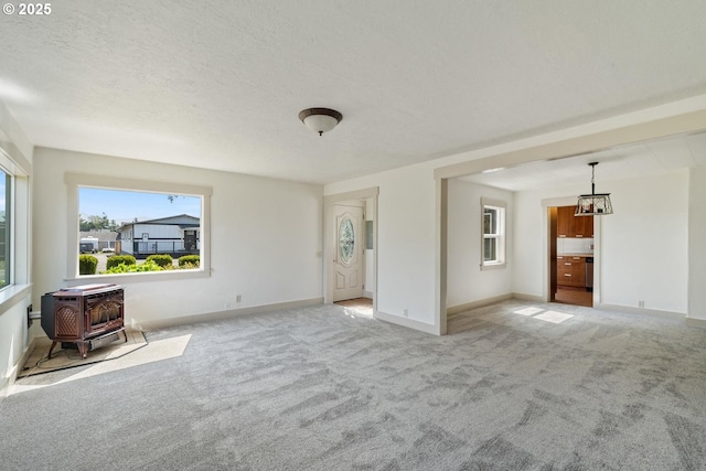 512 Evergreen Dr, Tillamook, OR 97141 - unfurnished living room with a wood stove, light carpet, baseboards, and a chandelier