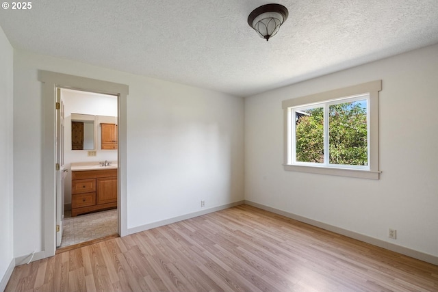 512 Evergreen Dr, Tillamook, OR 97141 - unfurnished bedroom featuring light wood-style flooring, baseboards, a textured ceiling, ensuite bathroom, and a sink