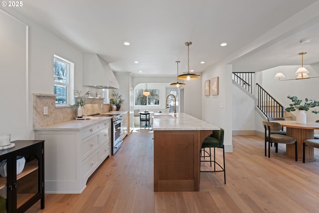 3660 SE Henderson St, Portland, OR 97202 - kitchen with custom exhaust hood, high end range, tasteful backsplash, a kitchen bar, and light wood finished floors