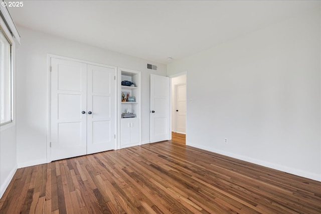 unfurnished bedroom featuring a closet, wood finished floors, visible vents, and baseboards