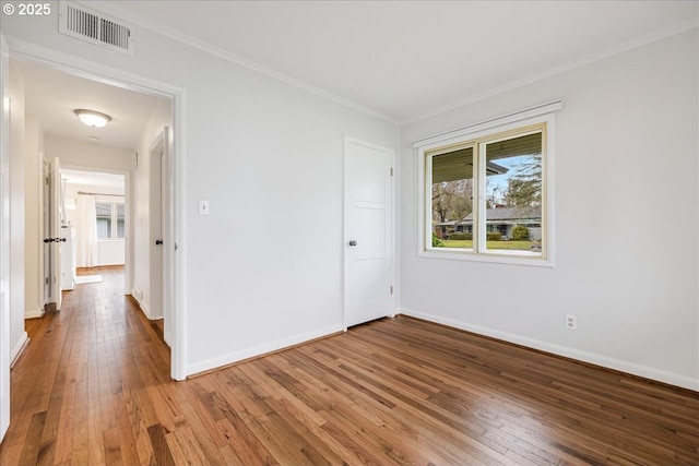 empty room featuring crown molding, hardwood / wood-style floors, visible vents, and baseboards