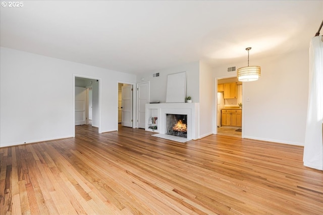 unfurnished living room featuring a fireplace with flush hearth, visible vents, light wood-style flooring, and baseboards