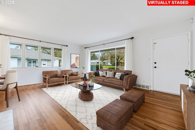 living room with wood-type flooring, visible vents, and baseboards