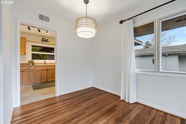 unfurnished dining area featuring a sink, wood finished floors, visible vents, and baseboards