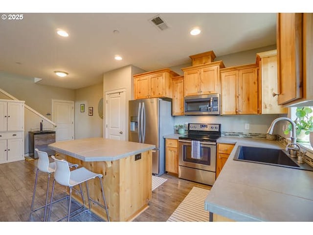 kitchen with stainless steel appliances, light countertops, a sink, a kitchen island, and wood finished floors